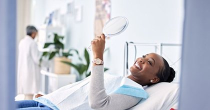 Happy dental patient looking at her smile in mirror