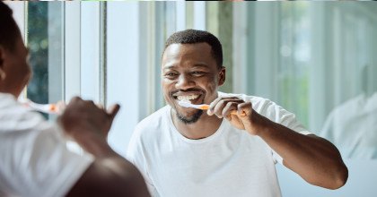 Man smiling while brushing his teeth in bathroom